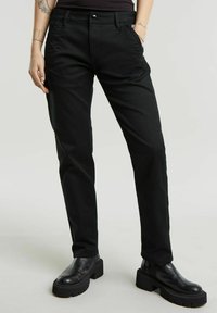 Pantalons noirs fuselés en coton avec une texture lisse. Comprend des poches avant, une fermeture avec bouton et zip, et des détails cousus.