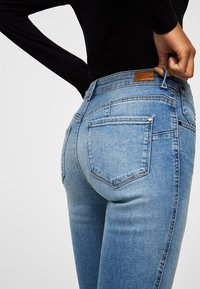 Vaqueros de denim de color azul claro con un diseño ajustado, costuras visibles y dos bolsillos traseros. Una etiqueta de cuero marrón está unida a la cinturilla.