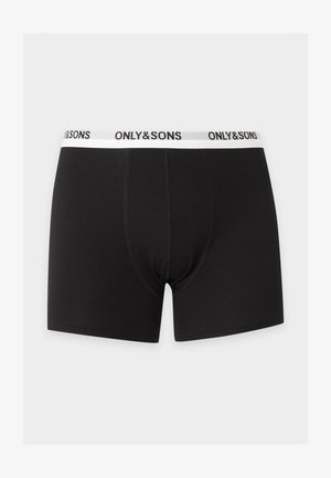 Schlanker dunkelhäutiger Mann steht barfuß da und trägt schwarze Boxer-Shorts mit weißem Bund und dem Markenaufdruck „ONLY & SONS“ vor weißem einfarbigem Hintergrund.