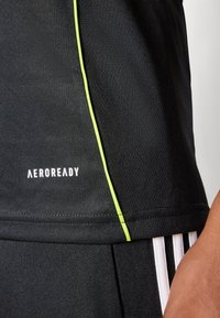 Fekete sportpóló, texturált anyagból, slim fit szabásban, neon zöld díszvarrással. A "AEROREADY" logó fehér színben látható.