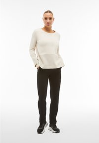 Light beige long-sleeve top with textured yoke and pockets, paired with black fitted pants and black sneakers with white soles.