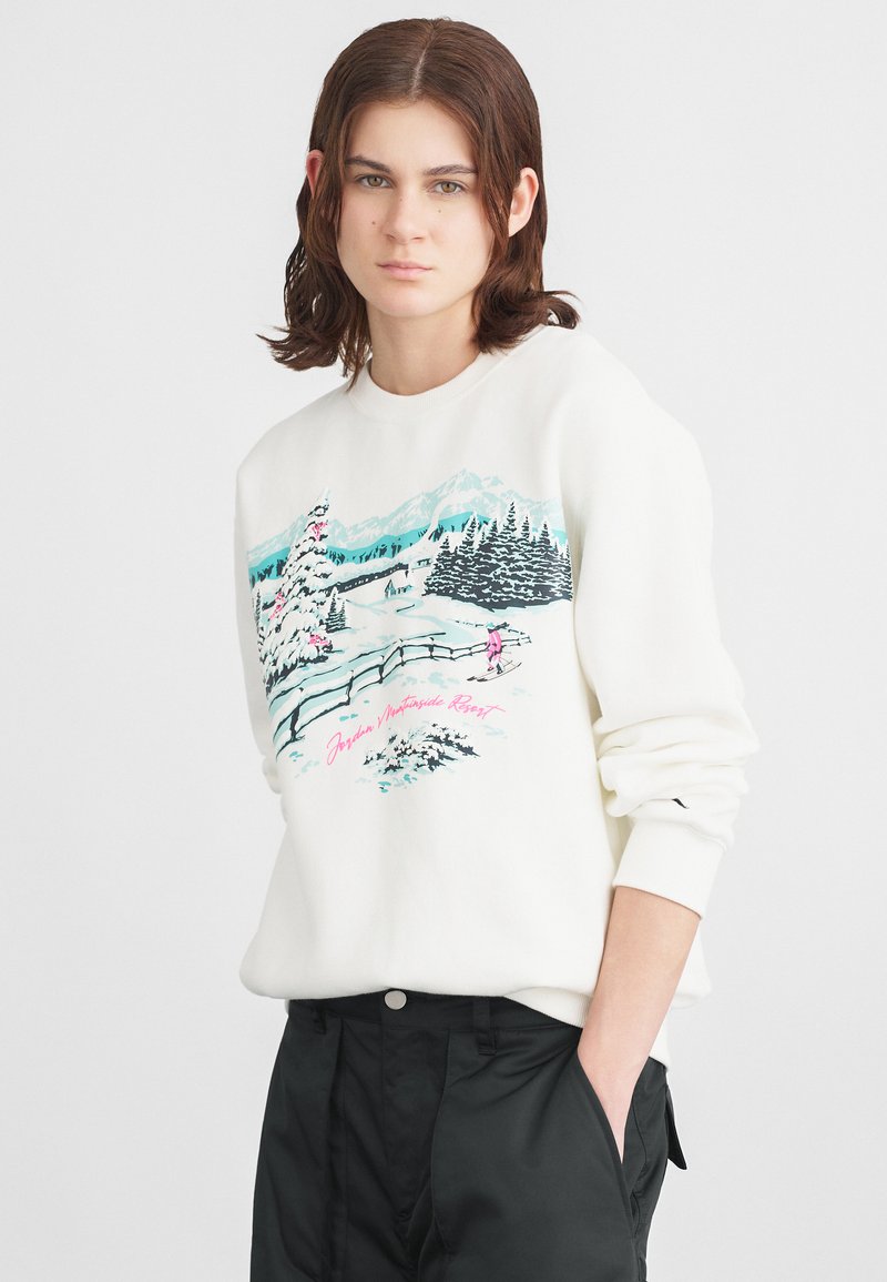Sweatshirt branco com uma gráfica de paisagem de inverno, apresentando uma árvore rosa e montanhas, em contraste com calças pretas de corte relaxado.