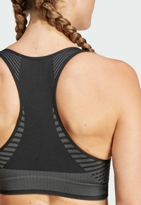 Svart sport-bh med ribbad textur, med en racerback-design och subtila grå randade detaljer längs axlarna och banden.