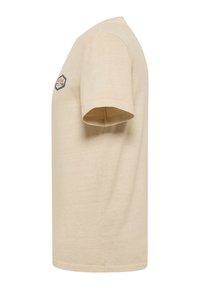 T-shirt beige à manches courtes avec un petit logo hexagonal sur la poitrine gauche, montré de côté.