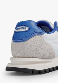 Zapatilla blanca con tacón de ante gris, detalles en cuero azul, superficie texturizada y suela de goma negra. Logotipo de SCALPERS en la lengüeta del tacón.