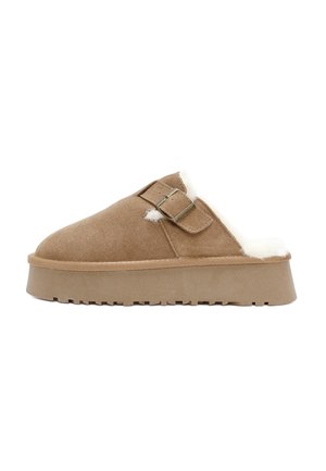 Chaussons en suède marron à enfiler avec une doublure en fourrure blanche, une semelle plate et deux accents de boucle sur le dessus. Texture douce partout.