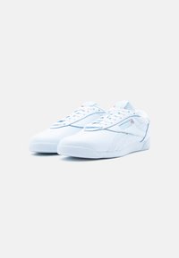 Ζεύγος καθαρών λευκών αθλητικών παπουτσιών Reebok με ανοιχτό μπλε και κόκκινες λογότυπες λεπτομέρειες σε λευκό φόντο.