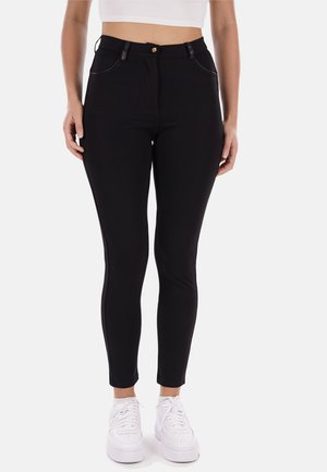 Jeans skinny neri a vita alta con cuciture argento, tasche anteriori e chiusura con un solo bottone. Abbinati a scarpe da ginnastica bianche.