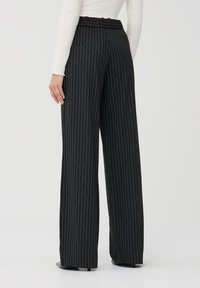 Pantaloni neri a gamba larga con righe bianche, cintura elastica e una texture morbida, abbinati a un top aderente a maniche lunghe bianco.