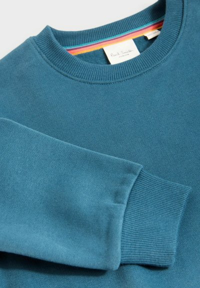 Felpa in cotone turchese con collo rotondo e polsini a coste, caratterizzata da un interno a righe multicolori sul colletto.