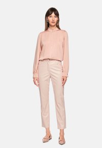 Rosa Satinbluse mit hohem Kragen, langen, aufgepufften Ärmeln und Knopfverschluss, kombiniert mit hellbeigen maßgeschneiderten Hosen und hellrosa Ballettschuhen.