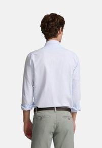 Camisa de manga larga azul claro con cuello abotonado, con rayas verticales, combinada con pantalones gris claro y un cinturón trenzado marrón.