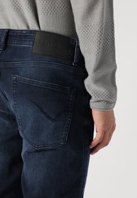 Tmavomodré džíny z denimu s textúrovaným šedým svetrom, ktorý má na páse čierny kožený štítok s nápisom "ONLY & SONS".