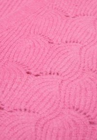 Roze, gestructureerde stof met een golvend patroon. Het materiaal lijkt zacht en pluisachtig, met zichtbare stikselaccenten langs het design.