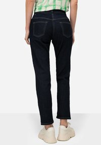 Jeans de mezclilla azul oscuro con un corte ajustado, que cuentan con dos bolsillos traseros y una cinturilla estándar. Los bajos están ligeramente doblados sobre zapatillas blancas.