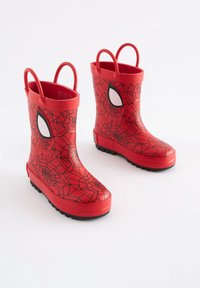 Bottes de pluie en caoutchouc rouge avec un motif de toile d'araignée noire, dotées d'accents d'yeux blancs et de deux poignées pour un enfilage facile. Semelle noire texturée.
