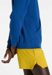 Blå huvtröja med ribbade muddar och en sidoficka, kombinerad med gula shorts med en liten sidoväv och en texturerad yta.