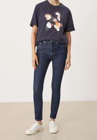 Camiseta de algodón navy con estampado abstracto multicolor; combinada con jeans skinny azul oscuro y zapatillas blancas. Atuendo simple y casual.