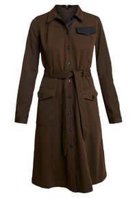 Ruskea puuvillasekoitetun kankaan paitamekko, jossa on pitkät hihat, etunapit, vyötärövyö, läpällä varustetut taskut ja musta kontrastipussiyksityiskohta.