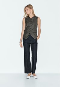 Bezramenný šedý svetr s pěti knoflíky, v kombinaci s tmavými džínovými kalhotami rovného střihu a bílými slip-on botami; hladká textura po celém povrchu.