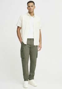 Korte mouwen crème knoopshirt over een wit T-shirt, gecombineerd met olijfgroene cargobroeken met zijzakken en witte sneakers.