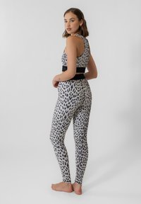 Løveprikket treningstøy sett med racerbakktopp og høy midje tights. Stoffet har en glatt tekstur, med en svart midjebåndakcent.