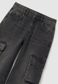 Zwart gewassen denim cargobroek met voorzakken, riemlussen, knoopsluiting en een klep cargozak op de dij.