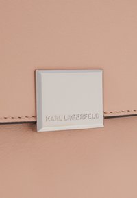 Světle růžová kožená kabelka s stříbrnou čtvercovou logo destičkou s vyraženým nápisem "KARL LAGERFELD" a jemnými stehy.