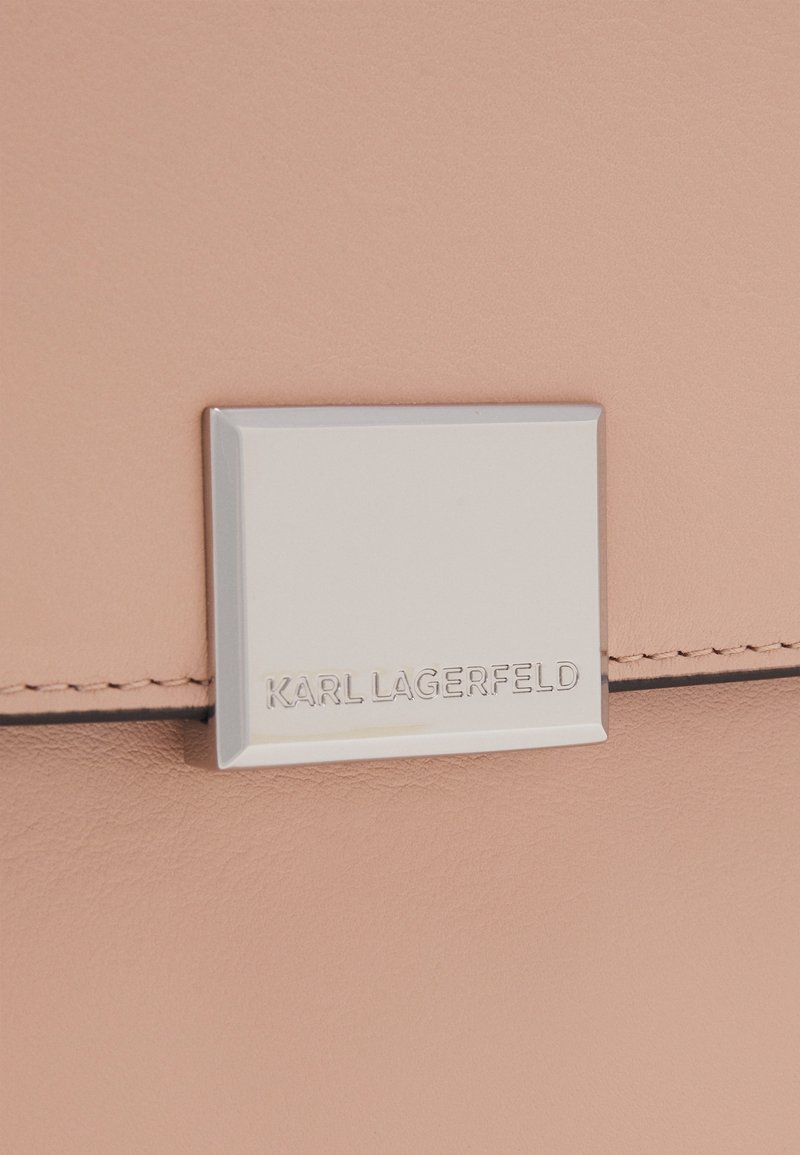Světle růžová kožená kabelka s stříbrnou čtvercovou logo destičkou s vyraženým nápisem "KARL LAGERFELD" a jemnými stehy.