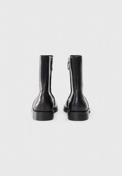 Botines de cuero negro con un diseño elegante, que cuentan con una cremallera lateral y un acabado suave. Suela de goma gruesa para mayor durabilidad.