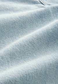 Tissu en denim bleu clair avec un tissage fin et texturé. Surface légèrement froissée montrant de subtiles variations de couleur et de motif.