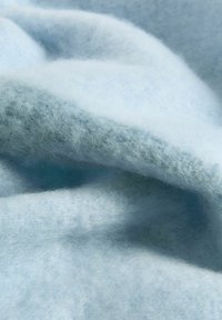 Pehmea helesinine kangas, millel on karvane, villataoline tekstuur, on kaunilt volditud ja varjude alla laskunud.