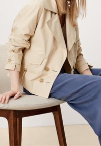 Beżowa marynarka podwójnie zapinana, wykonana z teksturowanej tkaniny, z dużymi klapami, dwoma przednimi kieszeniami i guzikami na rękawach.