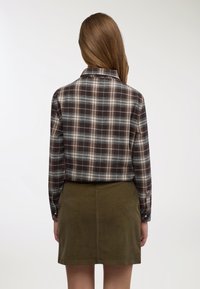 Camicia di flanella a quadri nei toni del marrone scuro, blu e crema, con maniche lunghe e colletto. Abbinata a una gonna in velluto a coste verde oliva.