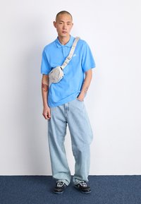 Svetlomodrá polo košeľa, voľné svetlé denimbové džínsy a čierne tenisky s bielymi detailami. Na tele je prehodená béžová crossbody taška.