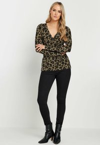 Leomuster Wickeloberteil aus olivgrünem und schwarzem Stoff, kombiniert mit schwarzen Skinny Jeans und Stiefeletten mit niedrigem Absatz. Lange Ärmel und V-Ausschnitt.