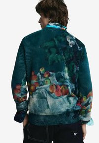 Svetre v textúrovanom tyrkysovom odtieni s farebným ovocným vzorom, rebrovaným dizajnom a voľným strihom. Dlhé rukávy s kontrastnými manžetami.