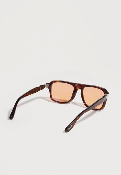 Καφέ ορθογώνια γυαλιά ηλίου με σχέδιο χελώνας και πορτοκαλί φακούς, ανοιχτά πάνω σε λευκή επιφάνεια.