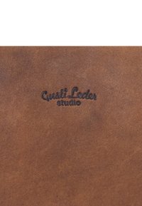 Nombre de la marca "Gusti Leder studio" en relieve sobre superficie de cuero marrón texturizado.