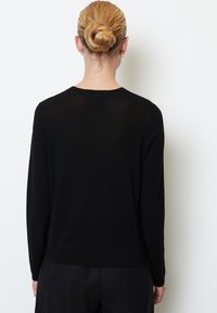 Zwarte trui met lange mouwen en een zachte textuur. Voorzien van een ronde hals en een geribbelde gebreide ontwerp, met een aansluitende pasvorm aan de achterkant.