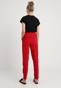 Red tailored trousers with a high waist and side pockets, paired with a black short-sleeve top. Smooth fabric with a slight sheen.