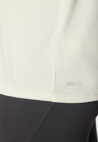 Lichte sportieve top van crèmekleur met een zachte textuur en DRYCELL-logo; gecombineerd met aansluitende zwarte leggings met contrasterende naden.