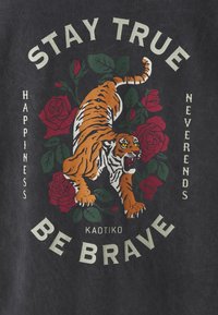 Camiseta gráfica negra con un tigre naranja rodeado de rosas rojas, con texto blanco que dice "MANTENTE FIEL", "SE VALIENTE" y "LA FELICIDAD NUNCA TERMINA".