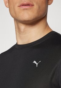Černé žebrované tričko s kulatým výstřihem, na levé části hrudníku s bílým logem Puma. Hladká textura a přiléhavý střih.