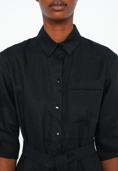Vestido preto de linho com decote tipo colarinho, mangas curtas, fecho frontal com botões, bolso no peito com bordado e um cinto amarrado na cintura.