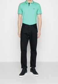 En mintgrön polotröja med svart krage och detaljer, parat med svarta raka byxor och svarta sneakers, med en mjuk textur.