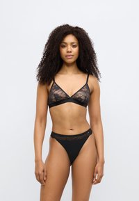 Μαύρο δαντελένιο μπουστάκι με λεπτές τιράντες και τριγωνικό σχήμα, σε συνδυασμό με μαύρο tanga σετ που διαθέτει δαντέλα κατά μήκος της ζώνης μέσης.