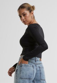 Svart tettsittende langermet topp med rund hals, kombinert med høyt liv lys blå denim jeans. Glatt tekstur, minimalistisk design.