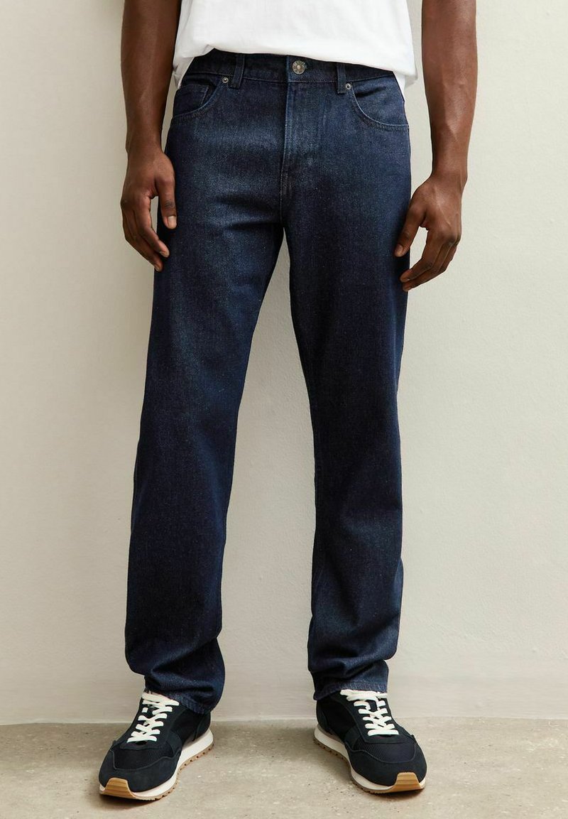 Jeans de denim azul oscuro con un corte recto, que cuentan con un cierre frontal de botón y cremallera, cinco bolsillos y un desgaste sutil.