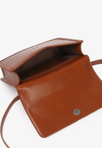 Sac bandoulière en cuir marron avec fermoir magnétique, ouvert pour montrer un compartiment principal unique et une poche intérieure sur fond blanc.